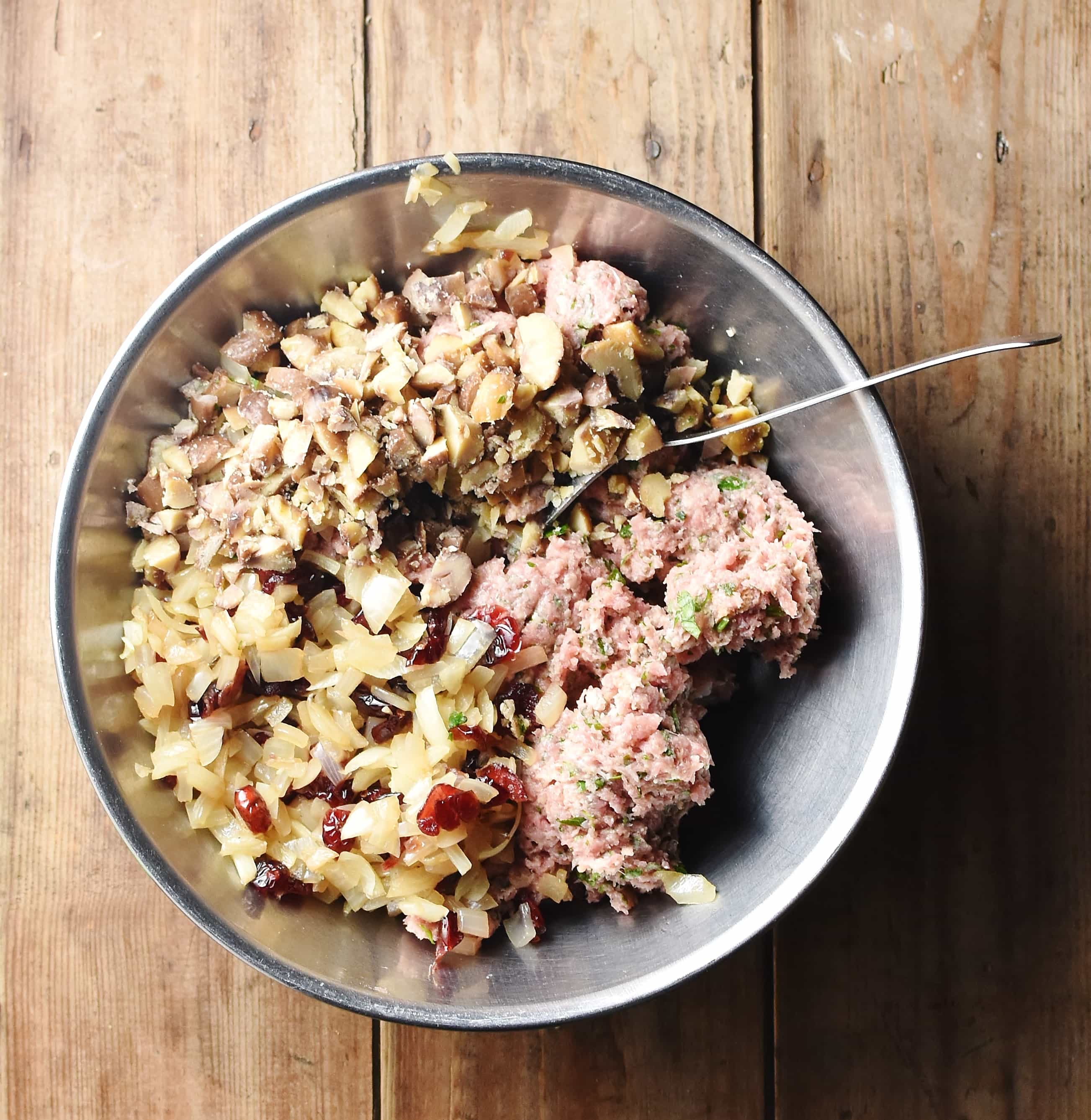 Minced meat, chopped onions and chestnuts inside large metal bowl with spoon.
