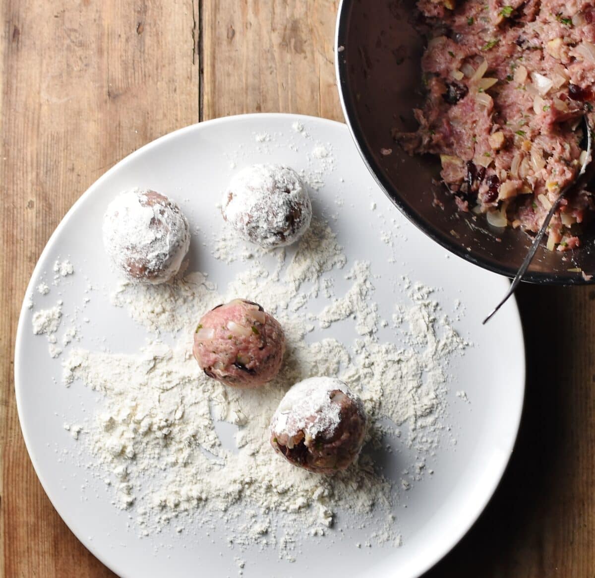 4 turkey stuffing balls coated in flour on large white plate, with stuffing mixture in metal bowl in top right corner.