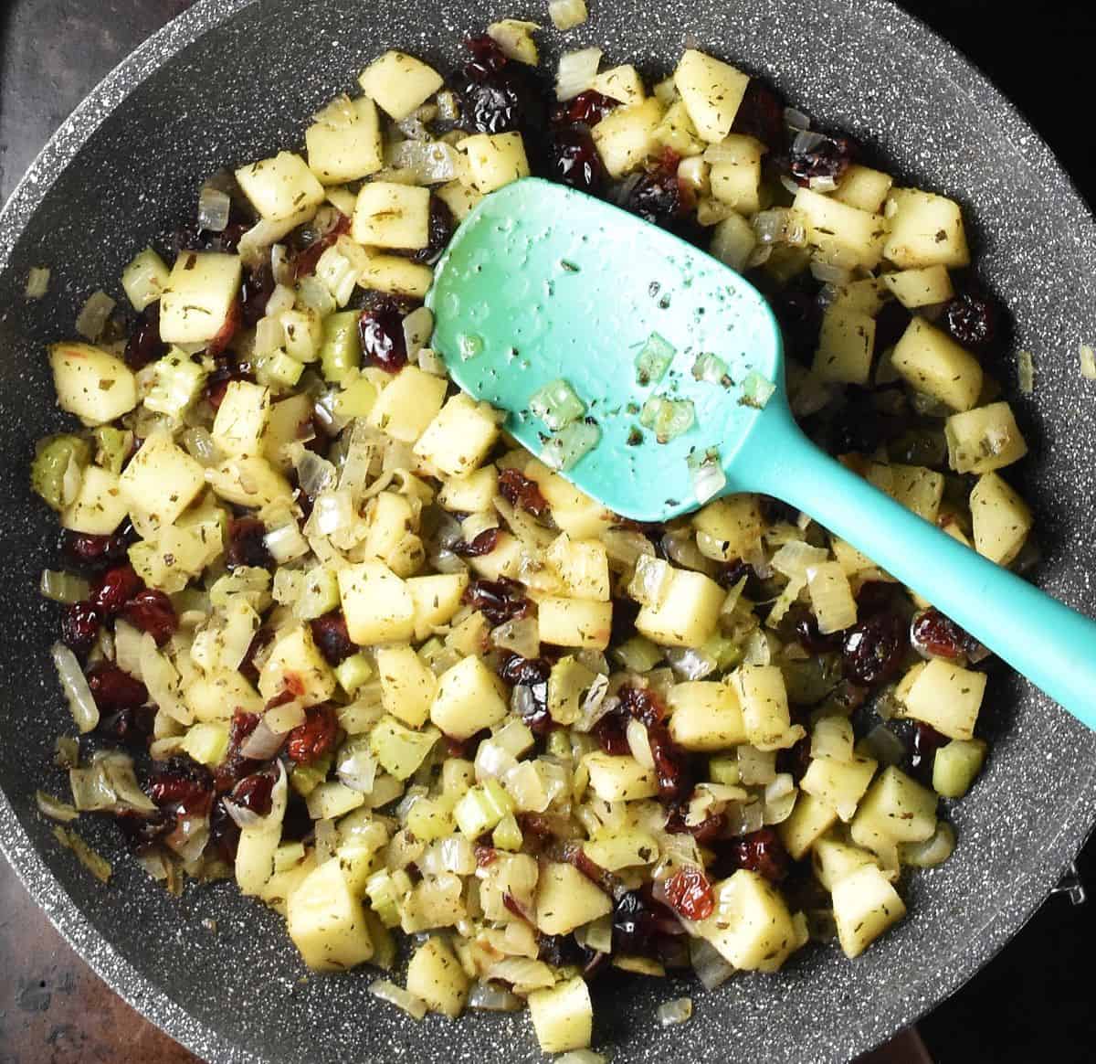 Mixture of chopped fruit and vegetables in grey pan with blue spatula.