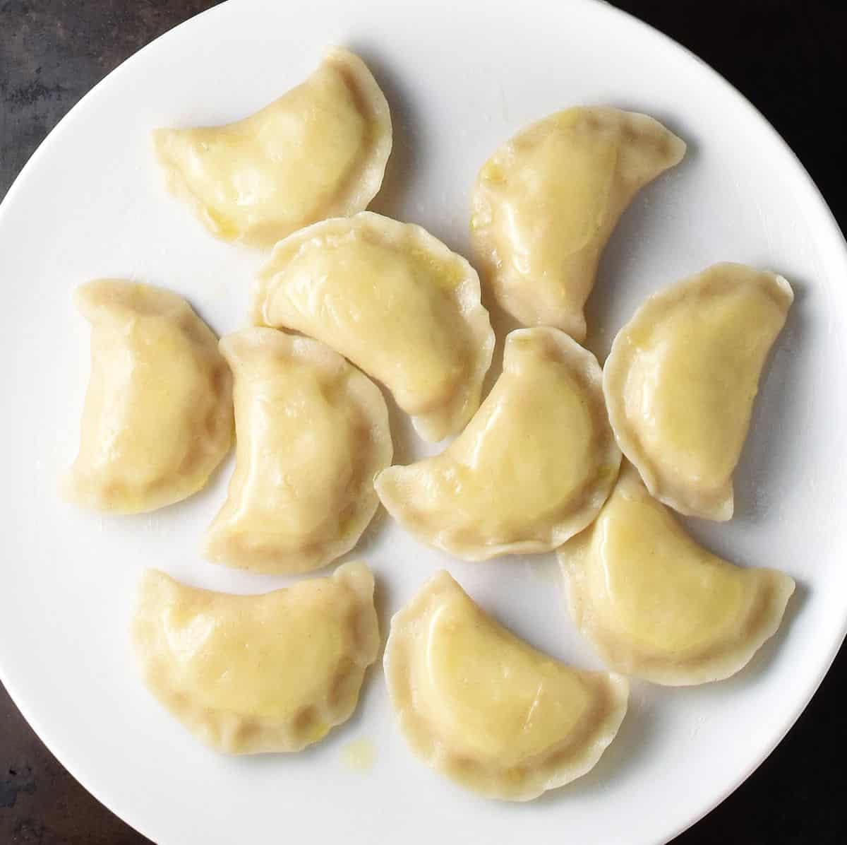 Boiled pierogi with cheese and potato on top of white plate.