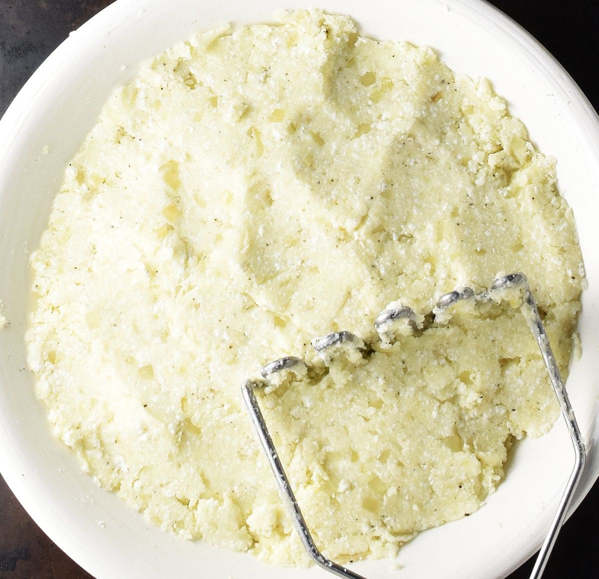 Creamy Polish pierogi ruskie filling mixture in white bowl with potato masher.
