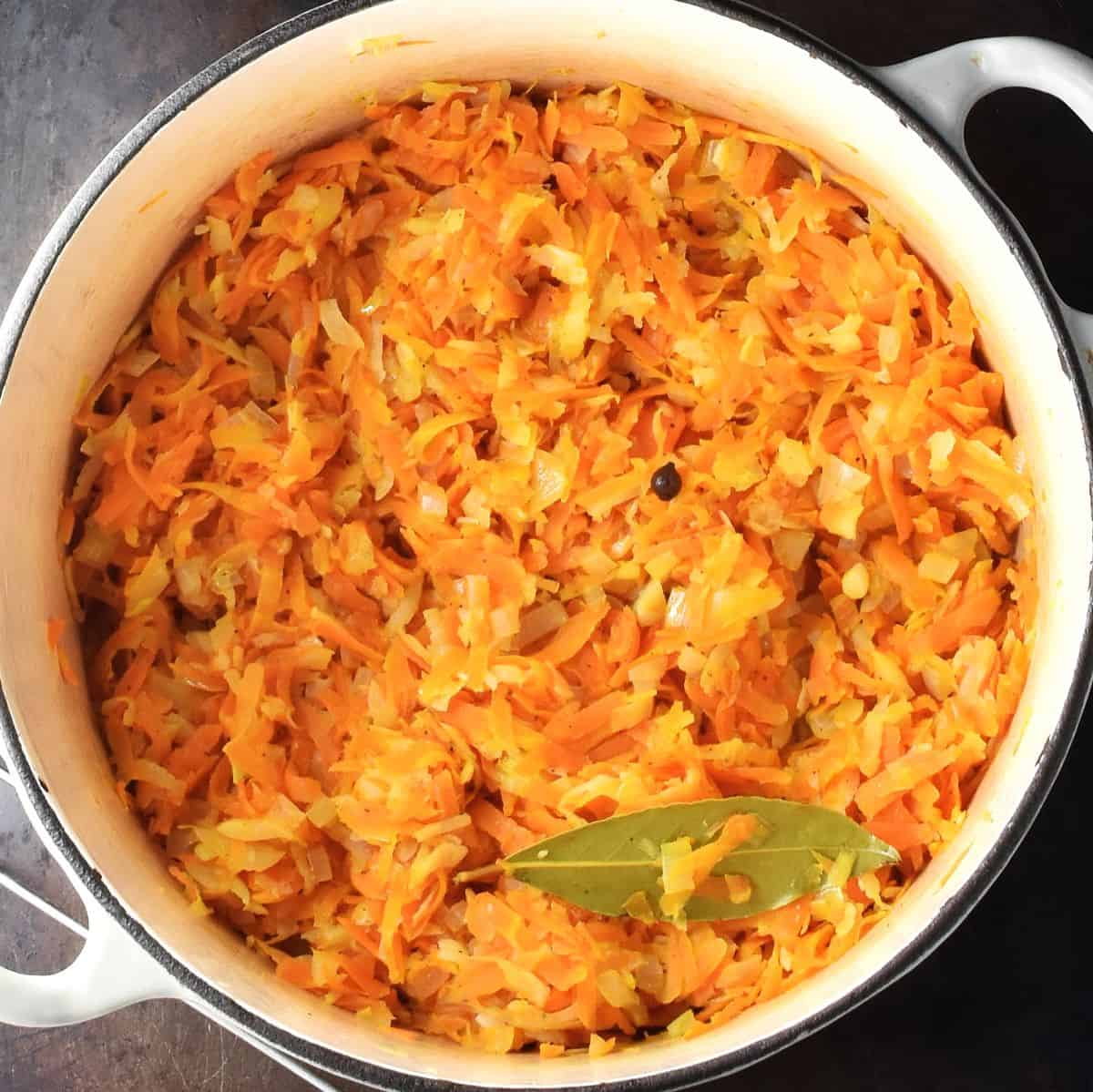 Top down view of root vegetable stew with bay leaf in white pot.