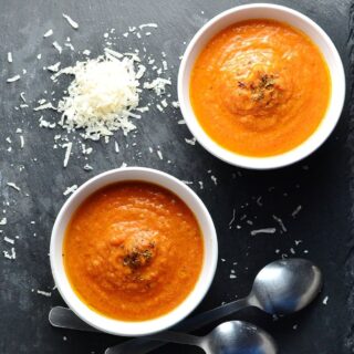 Top down view of creamy tomato soup in 2 white bowls with grated cheese and 2 spoons in background.