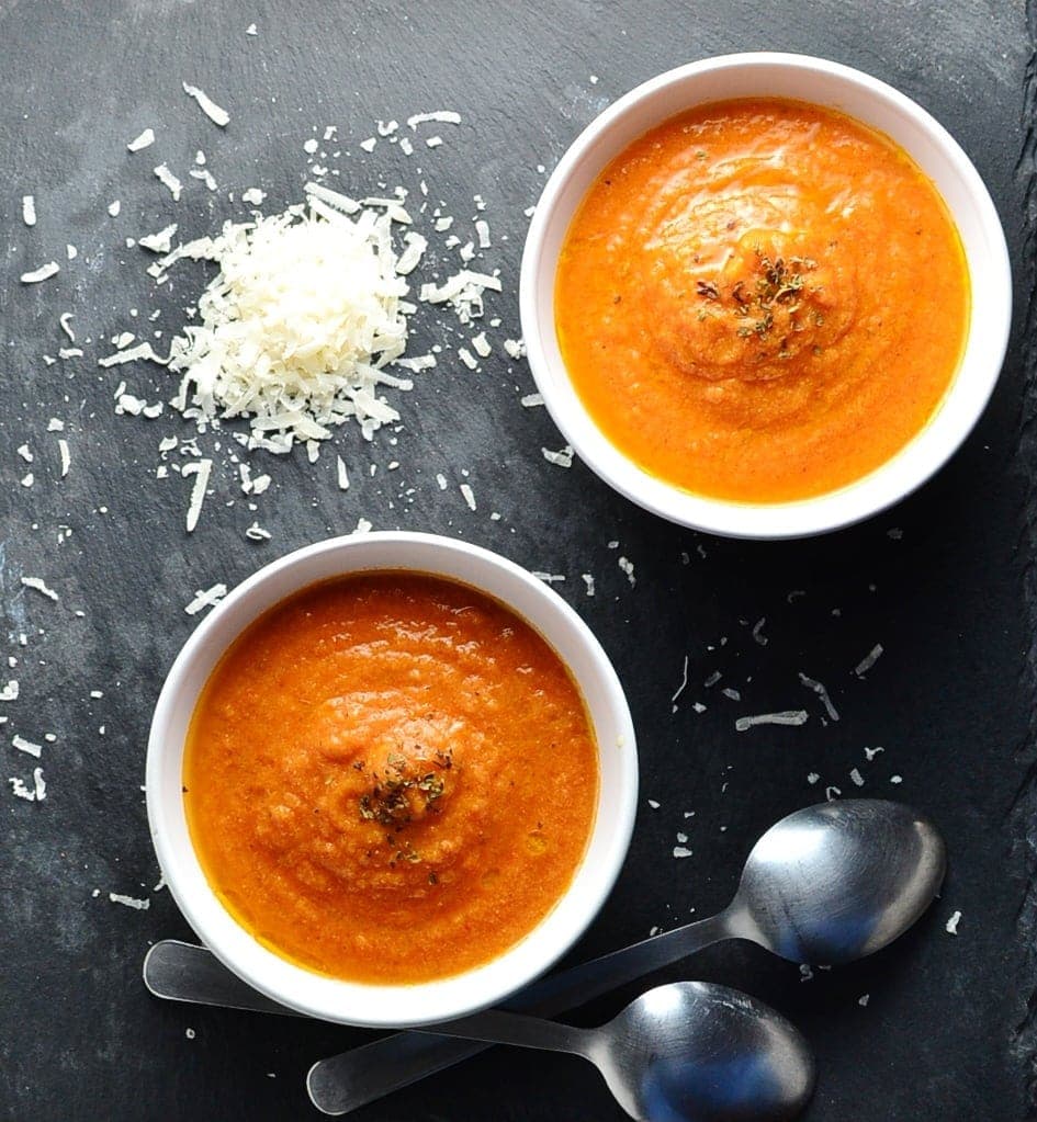 Top down view of creamy tomato soup in 2 white bowls with grated cheese and 2 spoons in background.
