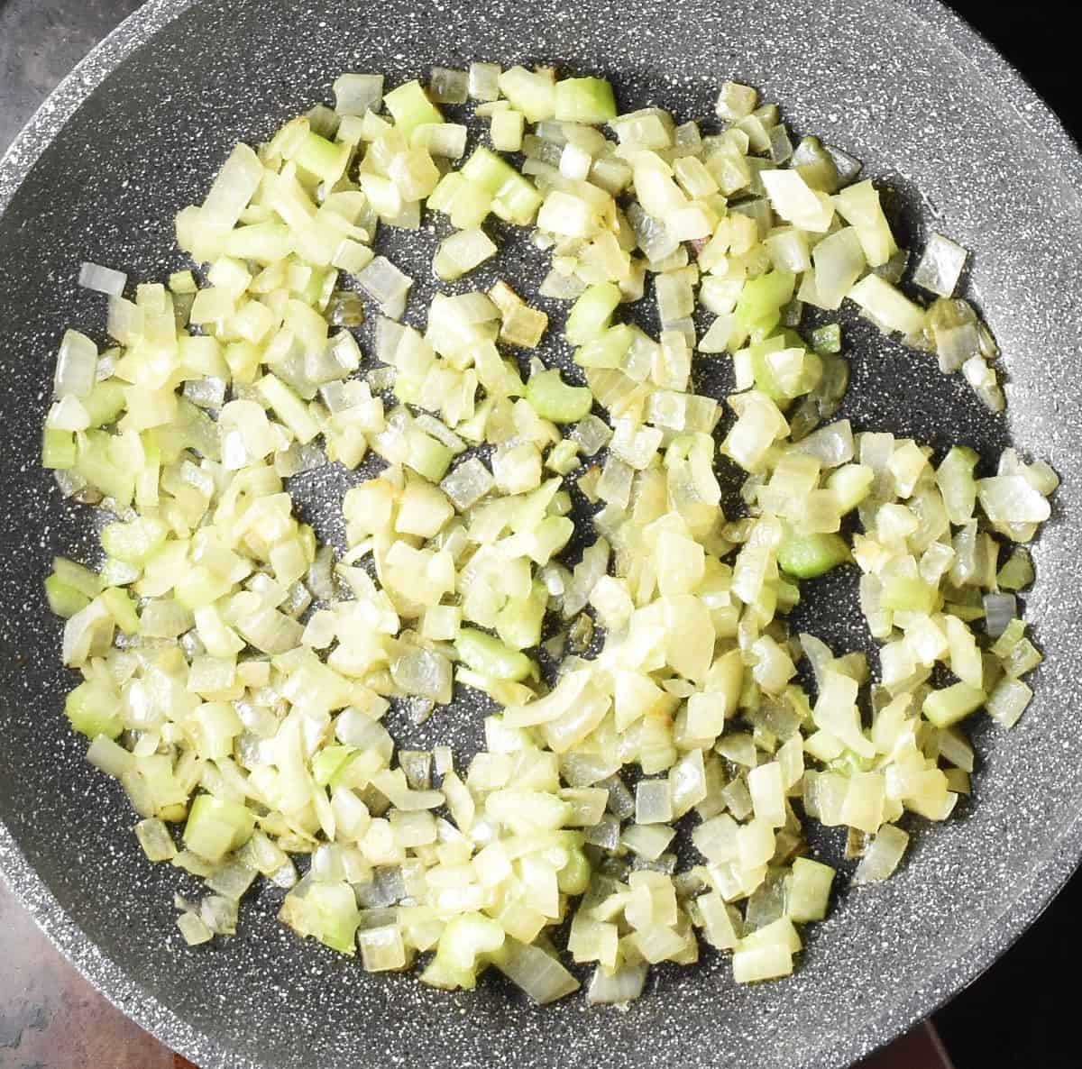 Chopped onion and celery sauteing in large grey pan.