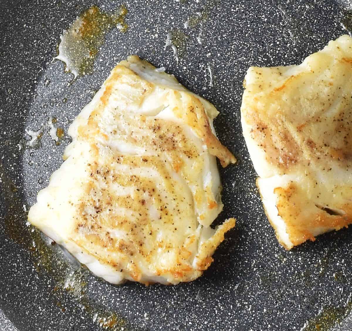 Top down view of 2 pieces of pan-fried fish in pan.