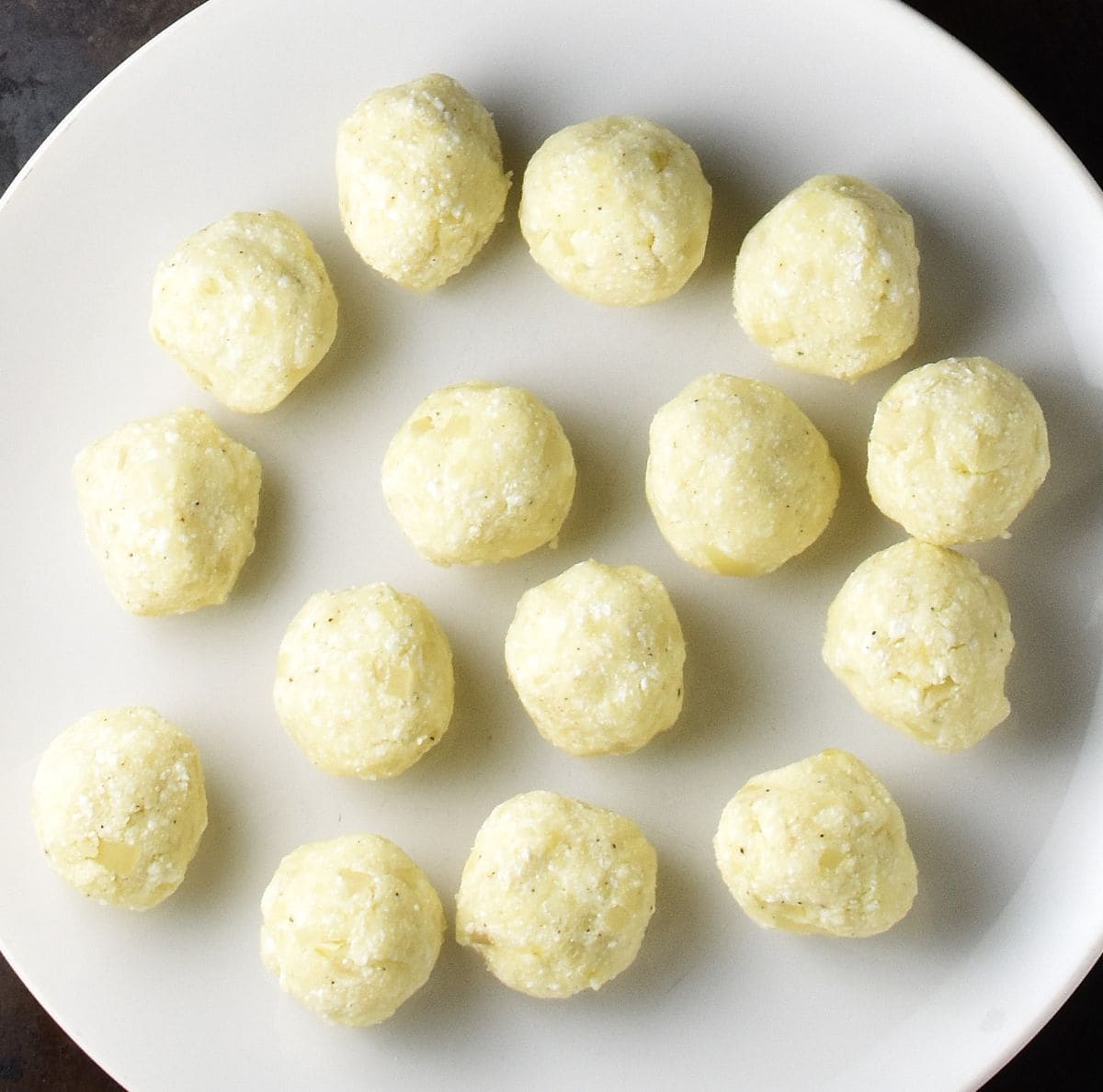 Polish potato cheese pierogi filling balls on white plate.