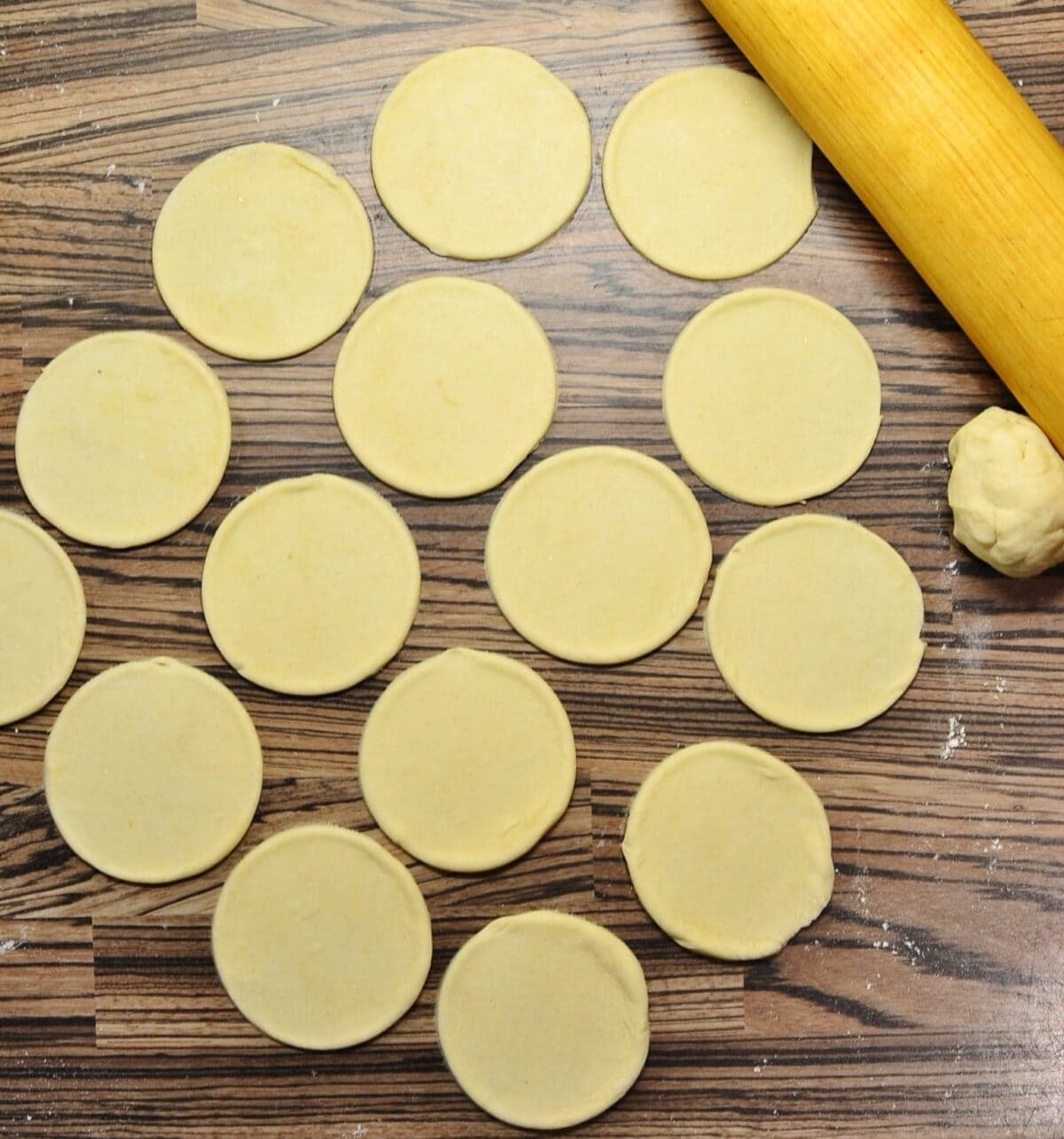 Rolled out pierogi dough with round dough shapes and rolling pin in top right corner.