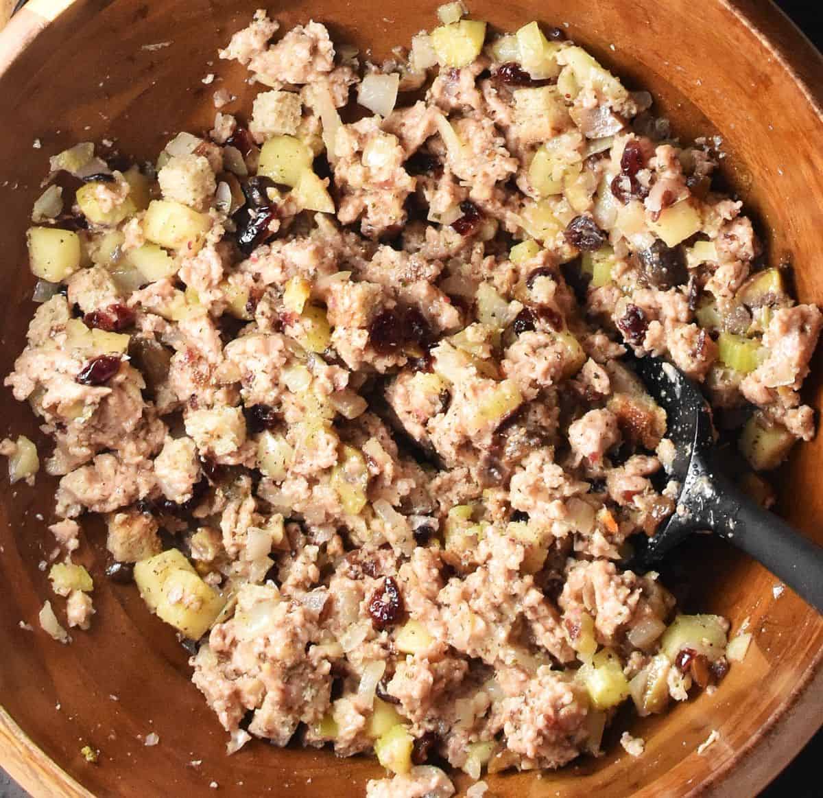 Top down view of vegan sausage stuffing mixture in wooden bowl with black spatula.