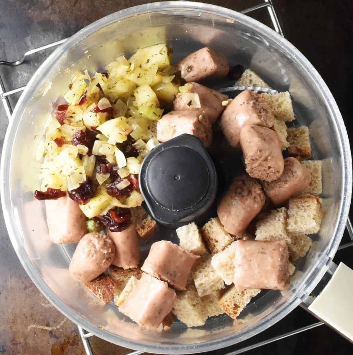Chopped vegan sausages and sauteed vegetables in food processor bowl.