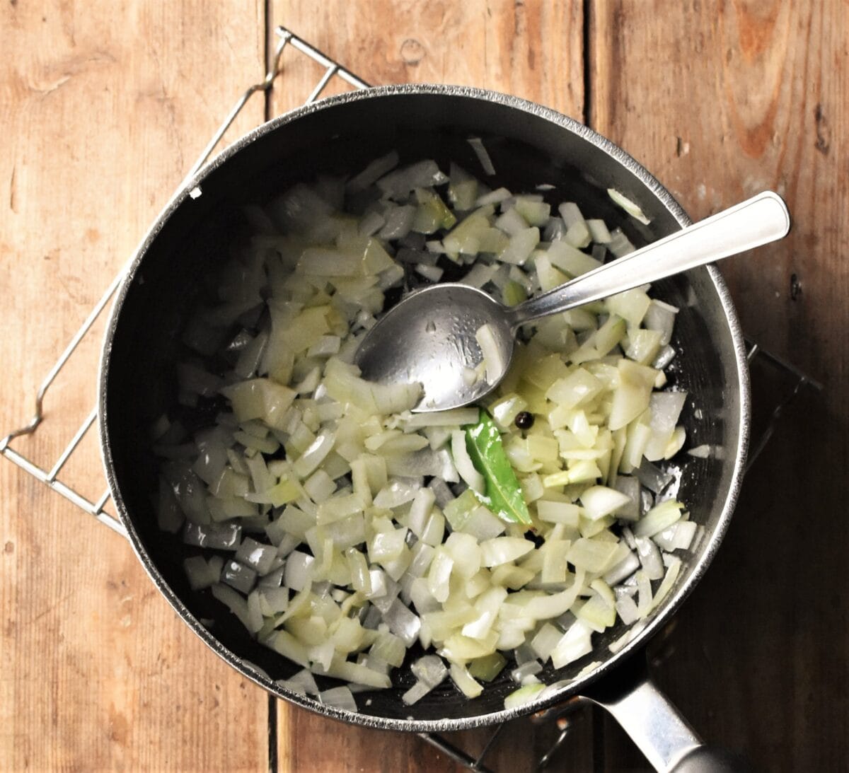 Chopped onions and bay leaf in large pot with spoon.