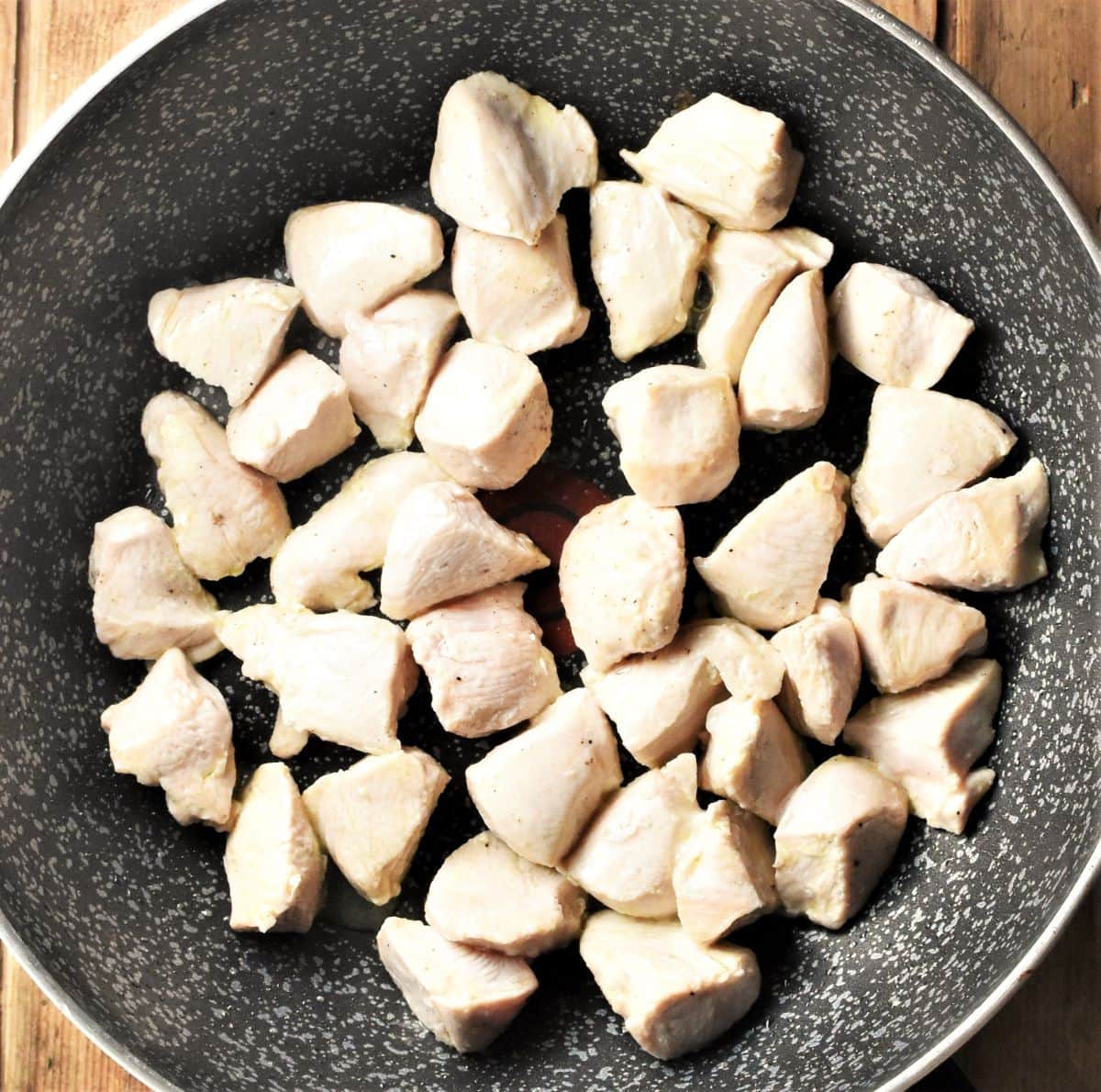 Cooking diced chicken in large pan.