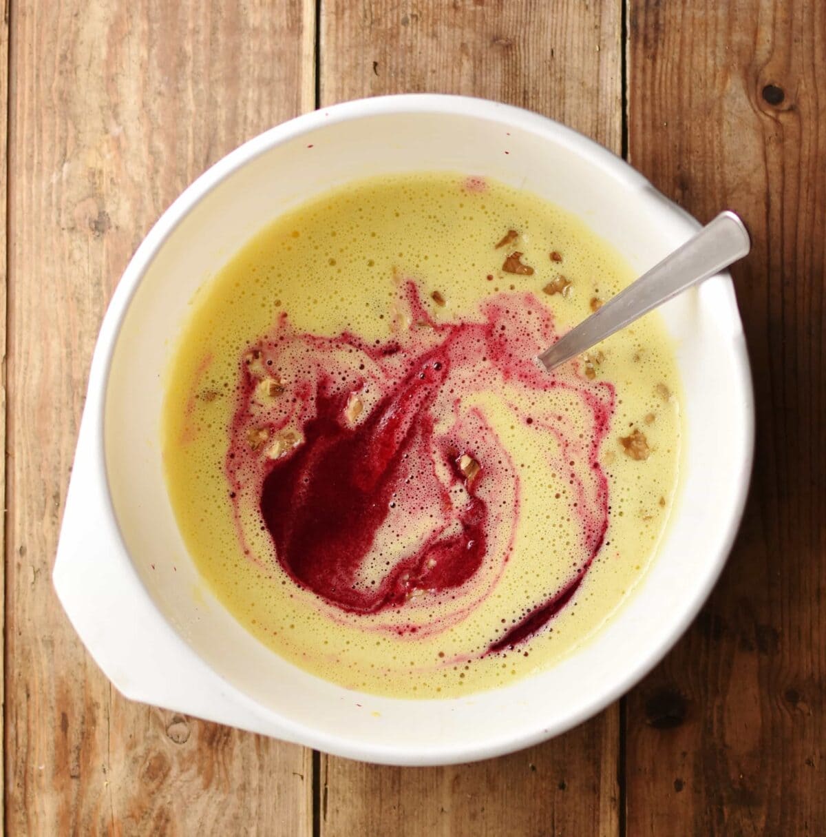 Egg mixture with partly visible beetroot mixture inside white bowl with spoon.