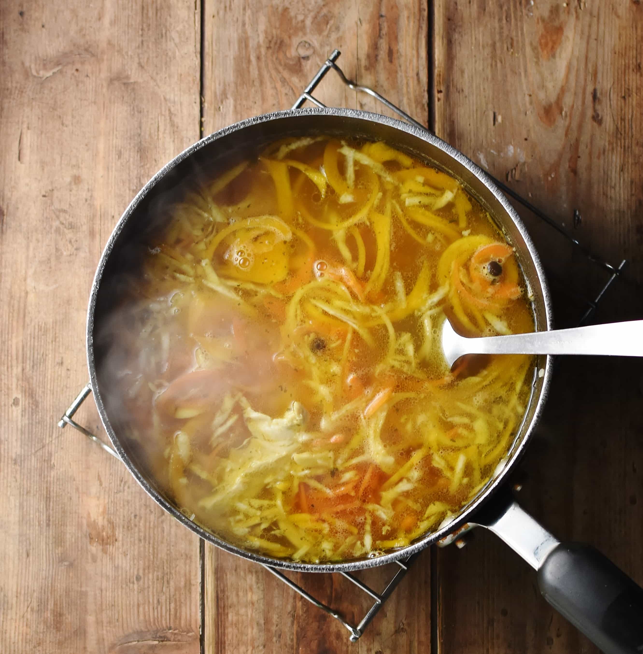 Spiralized vegetable chicken soup with steam in large pot with spoon.