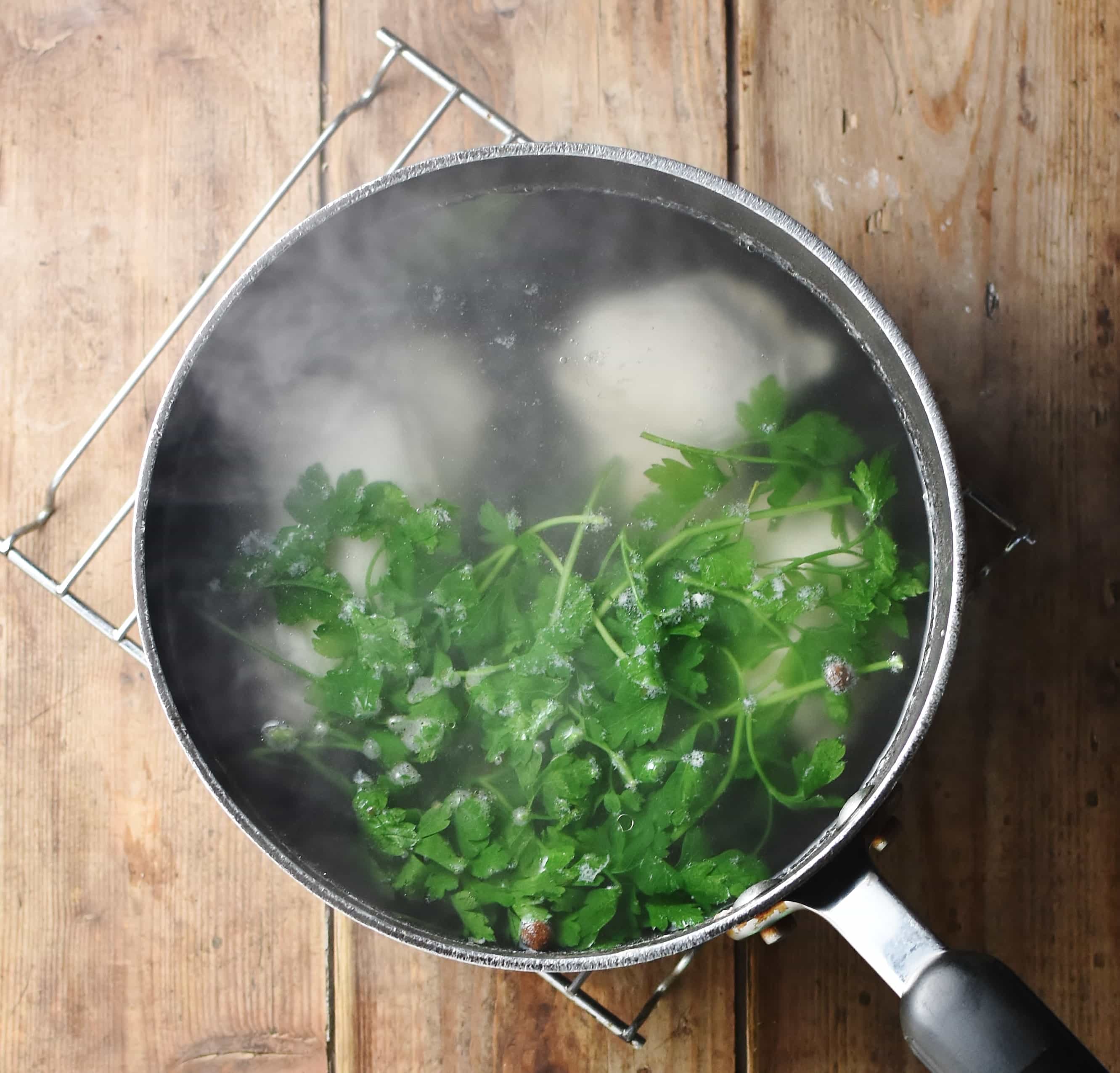 Chicken soup with parsley in large pot with steam coming out.