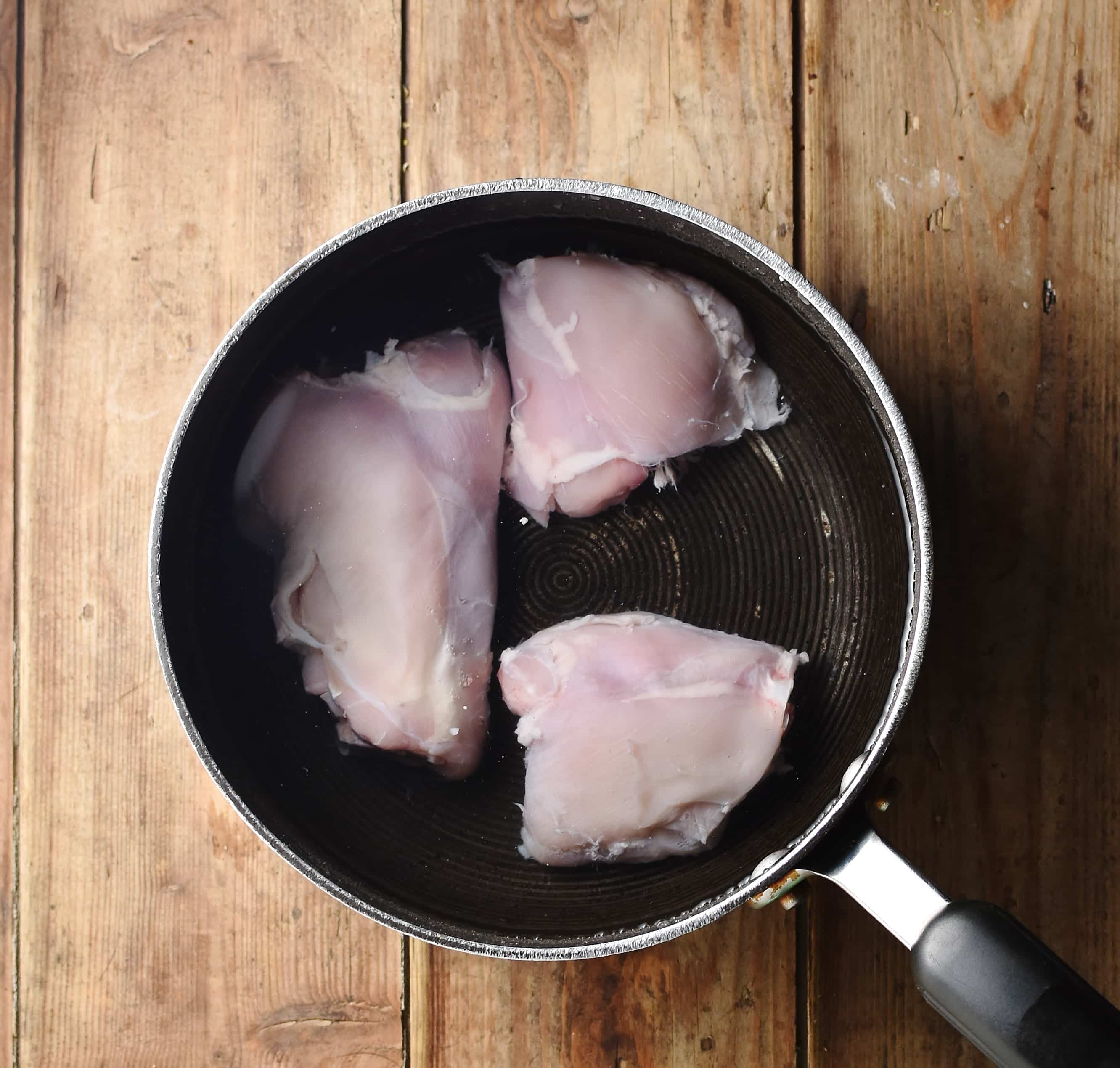3 skinless chicken thighs in pot with water.