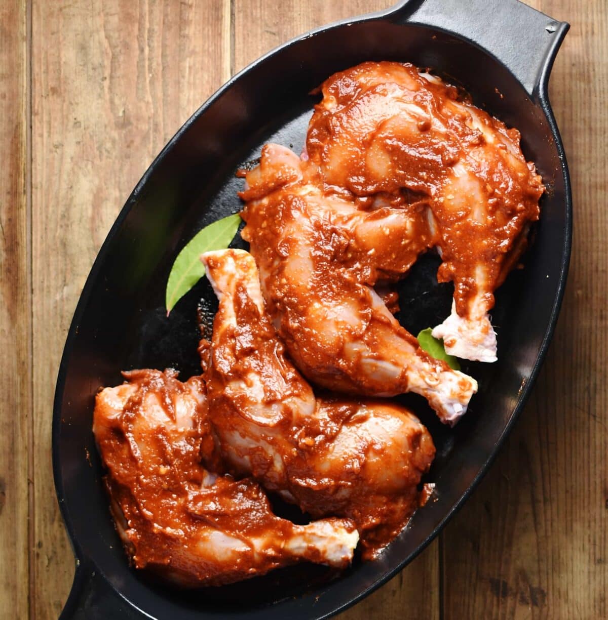 Chicken legs coated in marinade inside black oval dish.