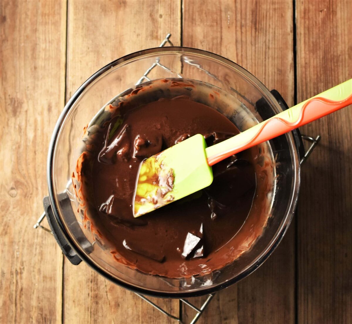 Melted chocolate in mixing bowl with green spatula.