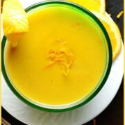 Orange sauce in round dish on white plate with slices of orange on dark brown surface.