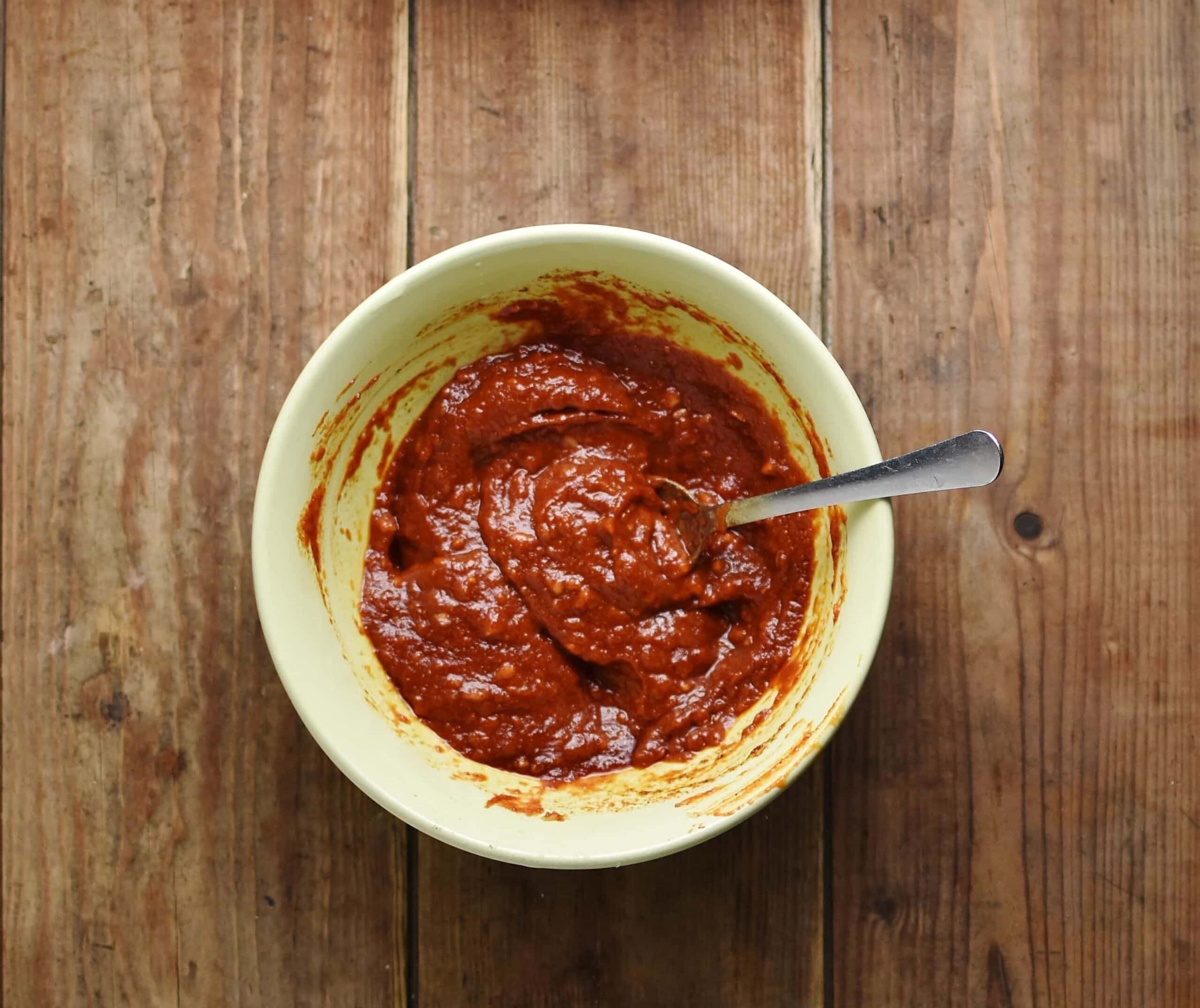 Pulled chicken marinade with spoon inside yellow bowl.