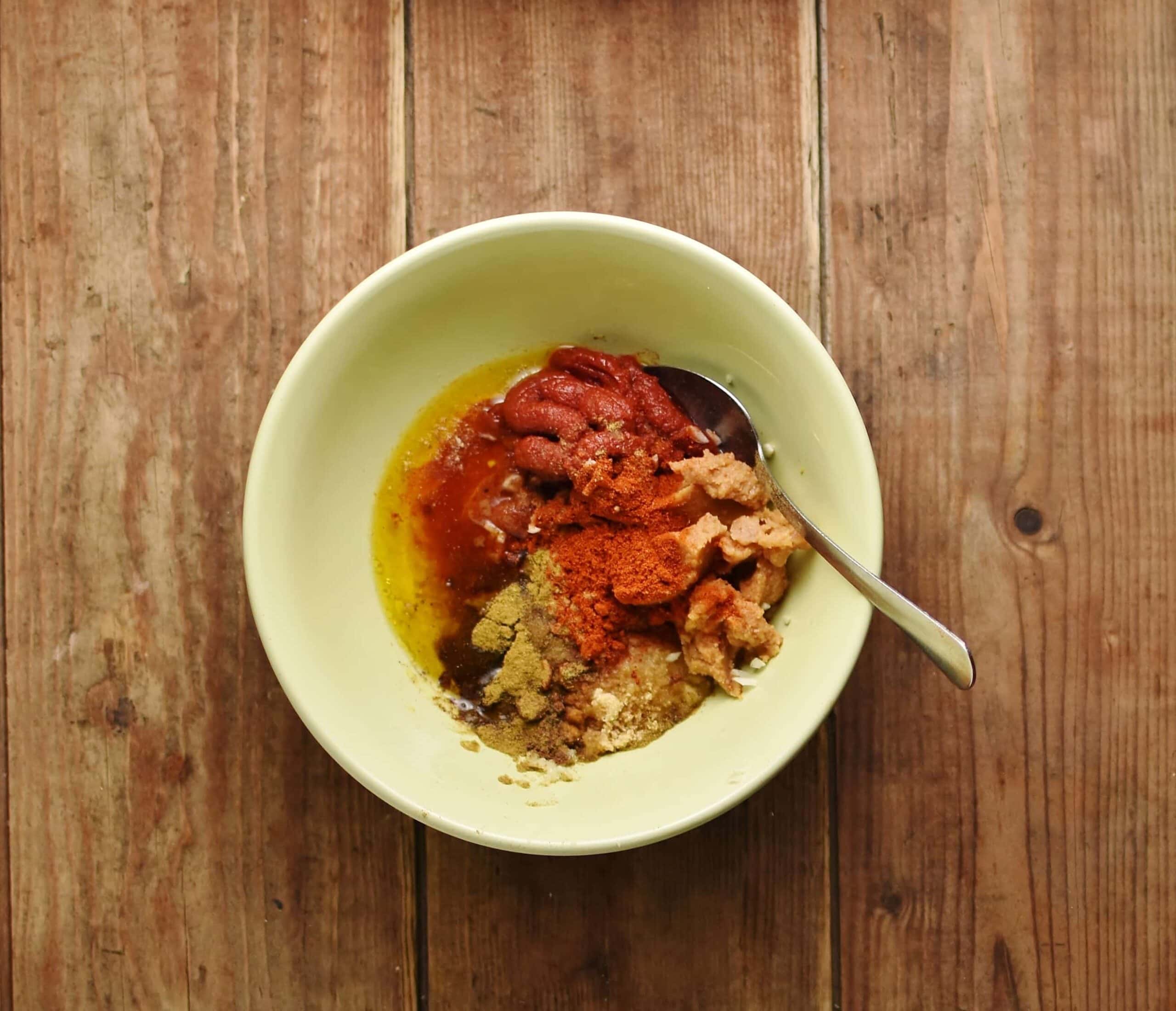 Chicken marinade spices with spoon inside yellow bowl.