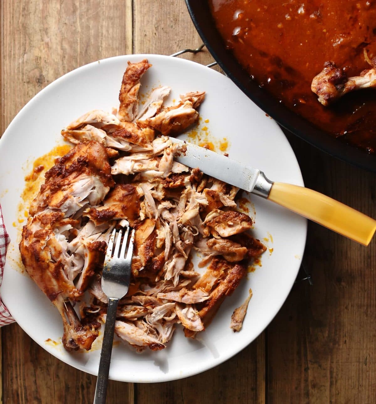 Shredded chicken with knife and fork on top of white plate.
