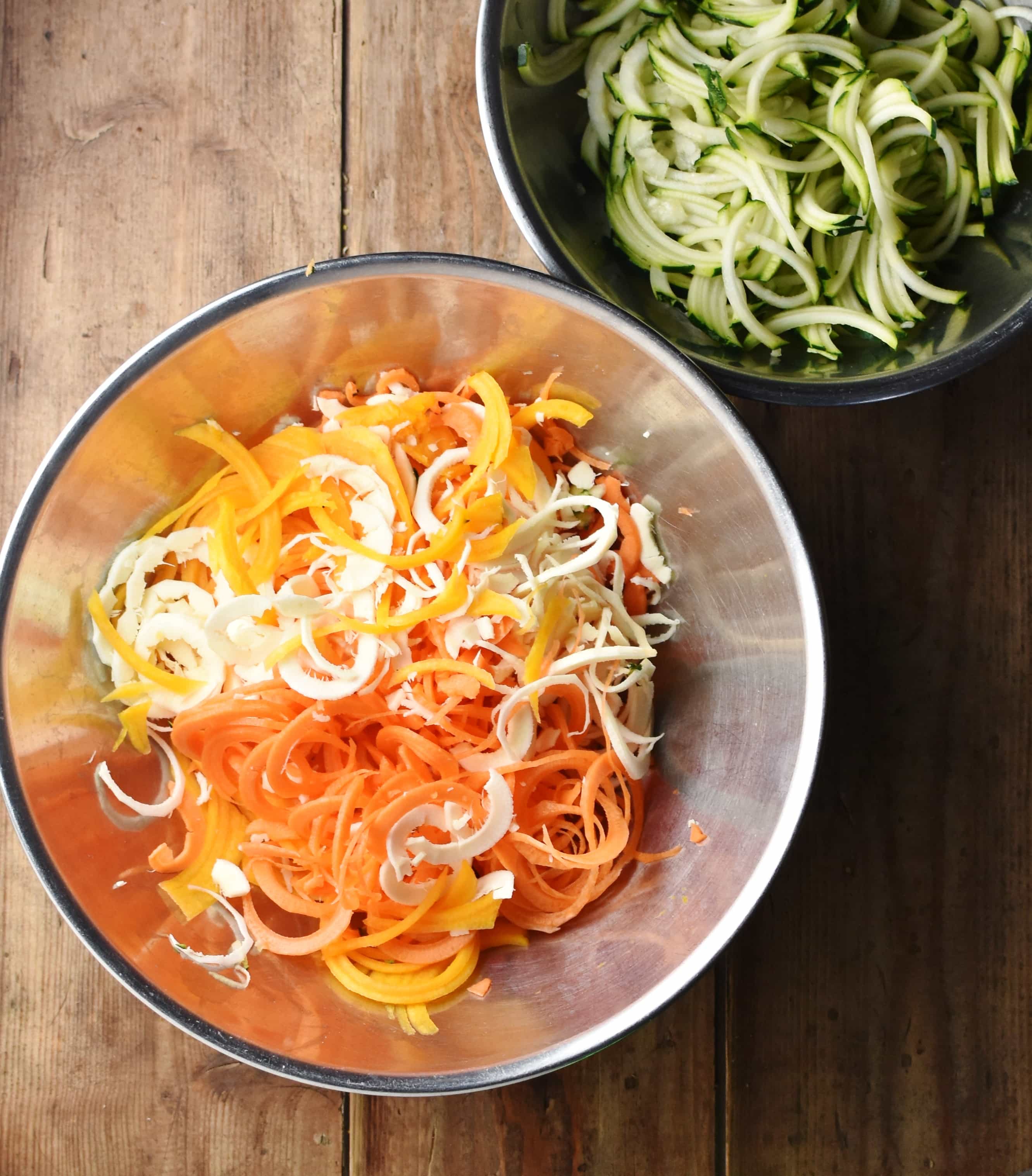 Spiralized vegetables in large metal bowl and zoodles in another bowl in top right corner.