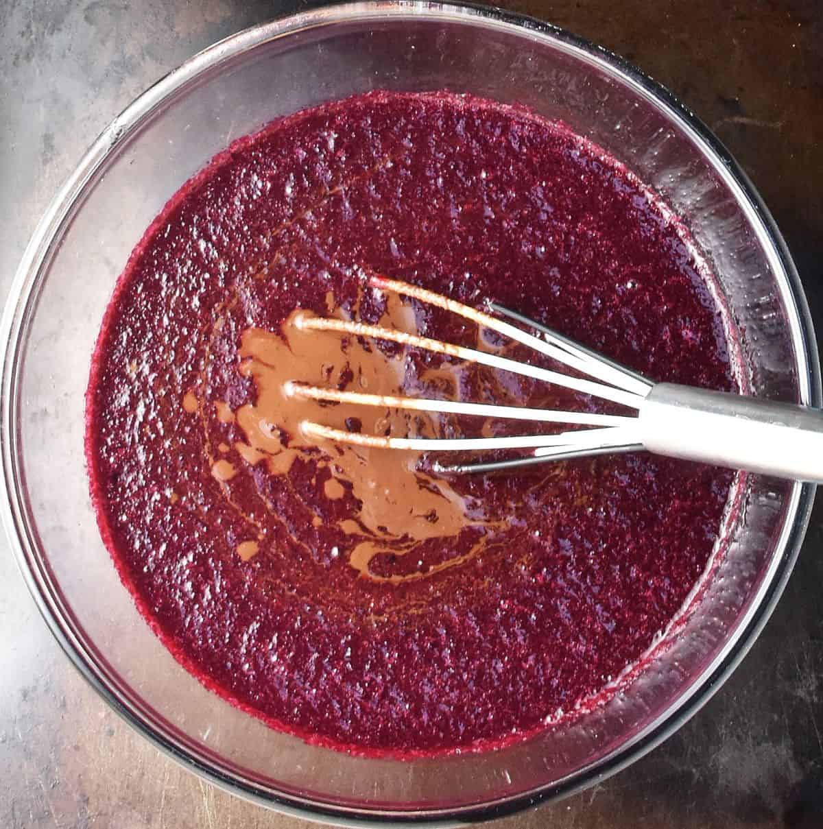 Top down view of beet mixture with melted chocolate and whisk in glass bowl.