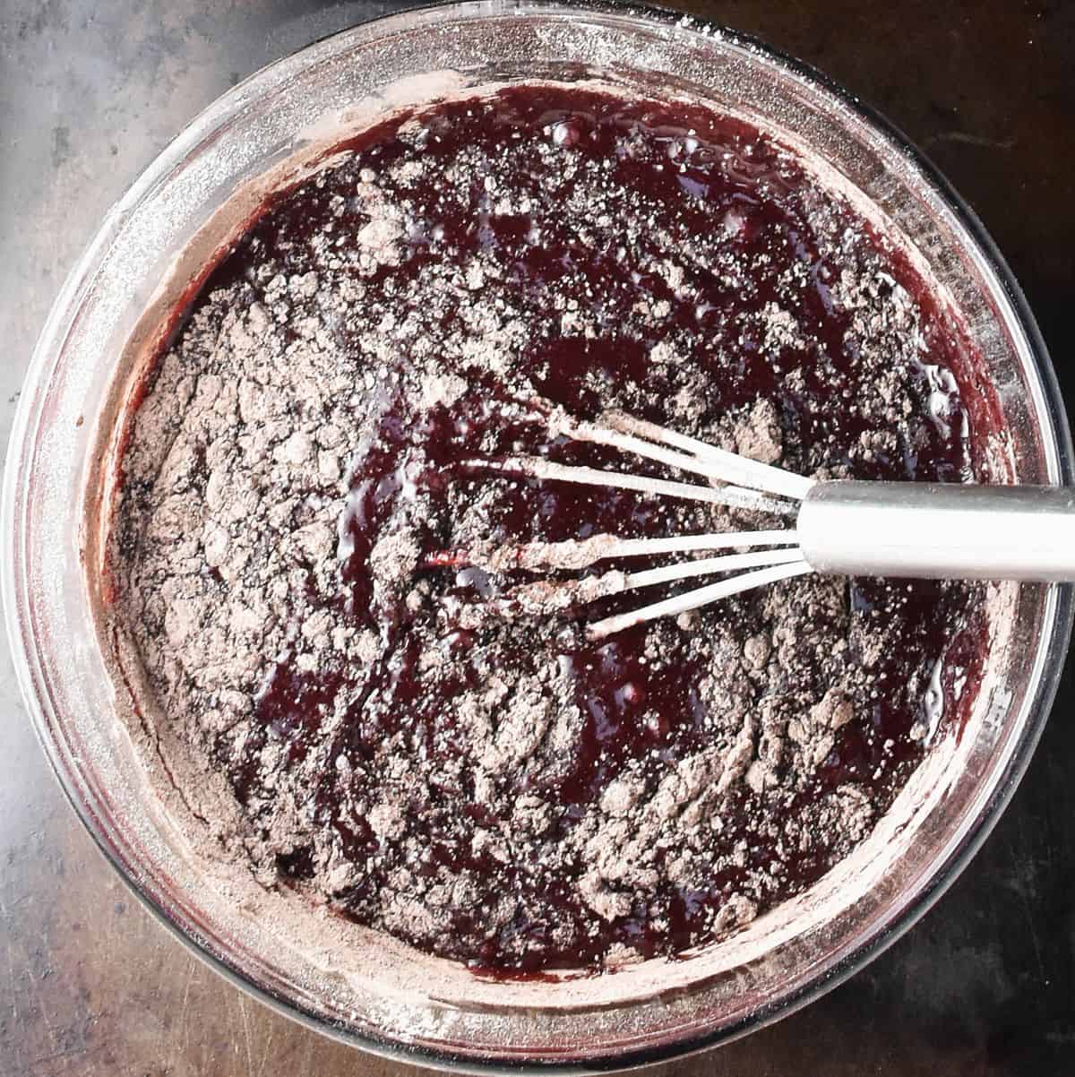 Beet brownies batter with flour visible and whisk in glass bowl.
