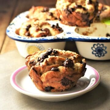 Side view of French toast muffin on small plate with muffins in pan in background.