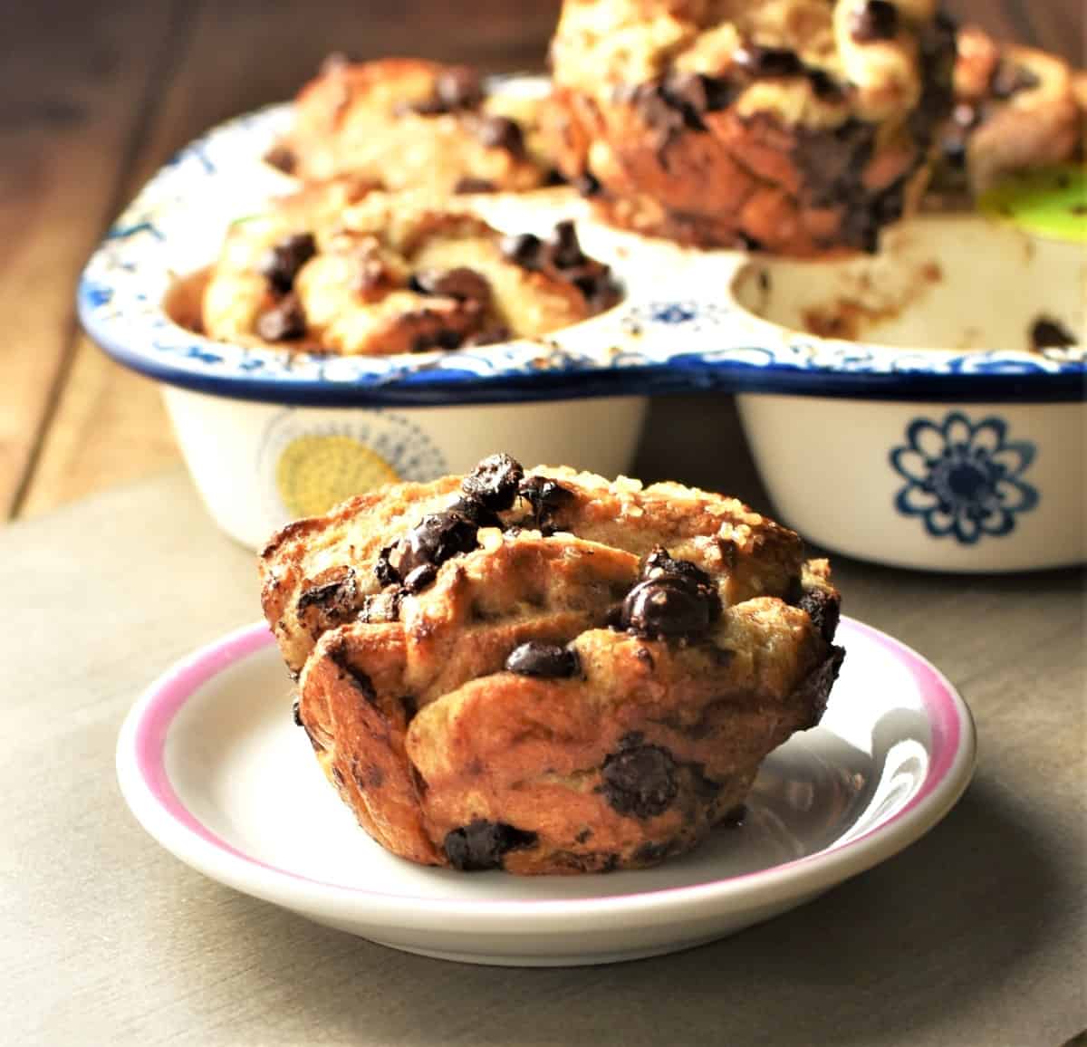 Side view of French toast muffin on small plate with muffins in pan in background.