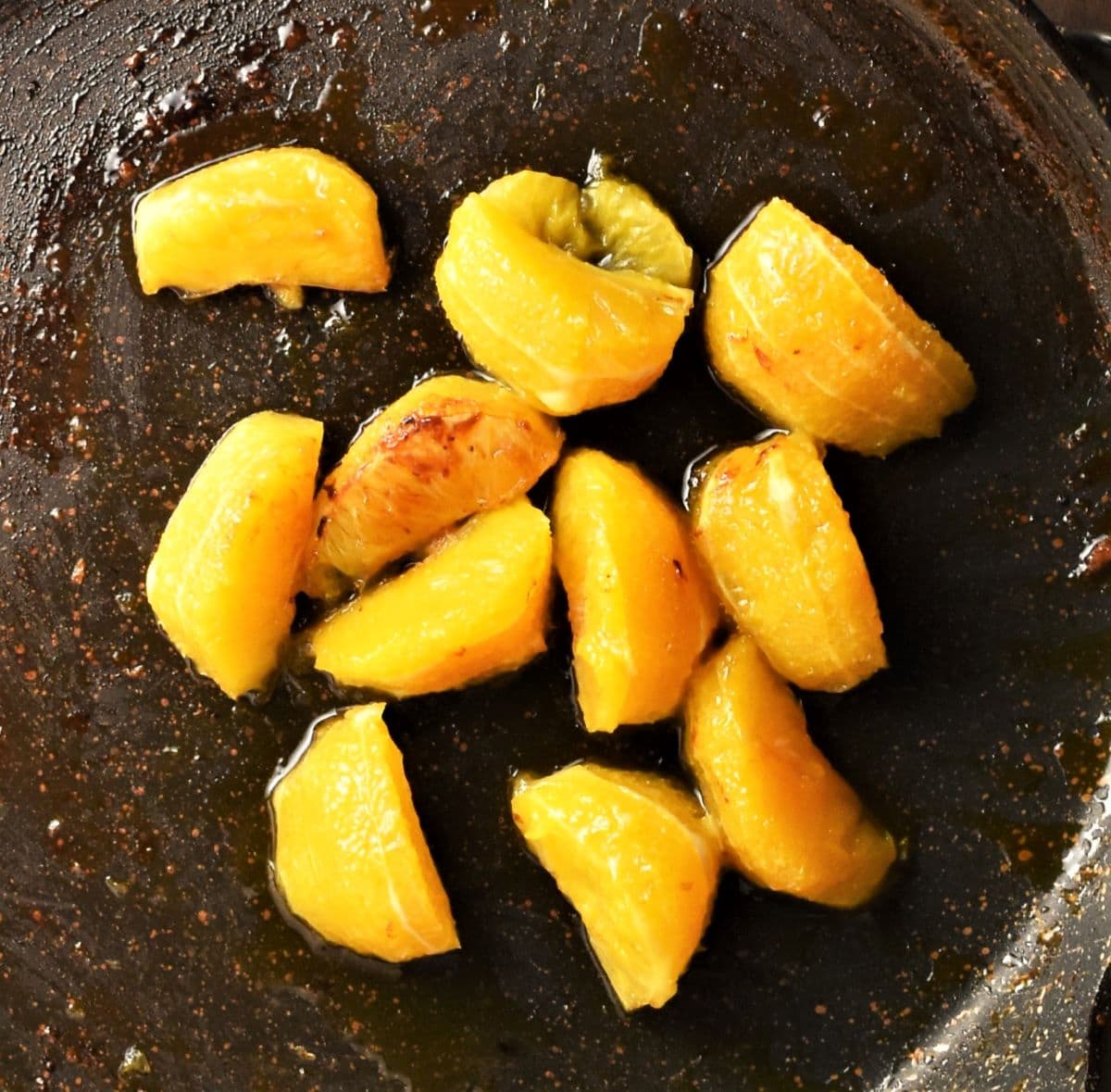 Frying peeled orange wedges in pan.