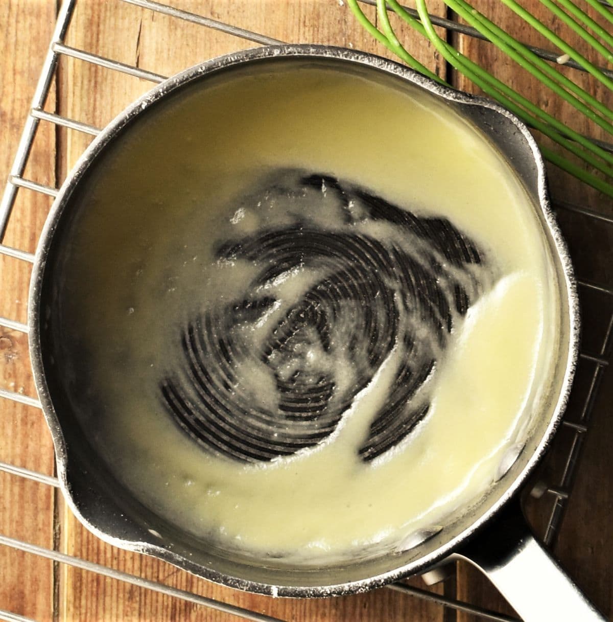 Making roux mixture in saucepan with green whisk in top right corner.