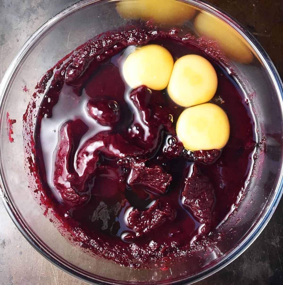 Top down view of beet mixture and 3 raw eggs in glass bowl.