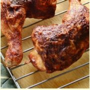 Close-up view of crispy chicken leg quarters on top of wire rack with lime wedges.