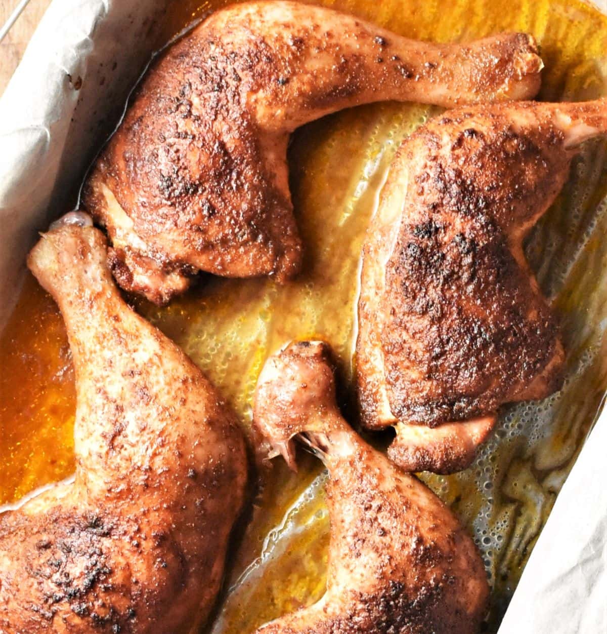 Close-up view of 4 crispy chicken legs in roasting pan.