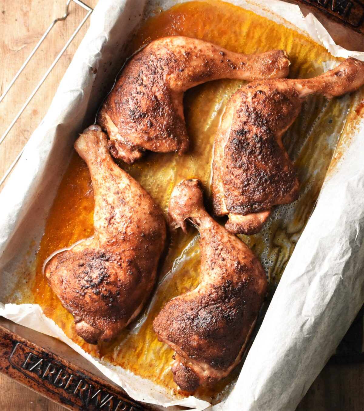 4 crispy baked chicken leg quarters and juices in roasting pan lined with parchment paper.
