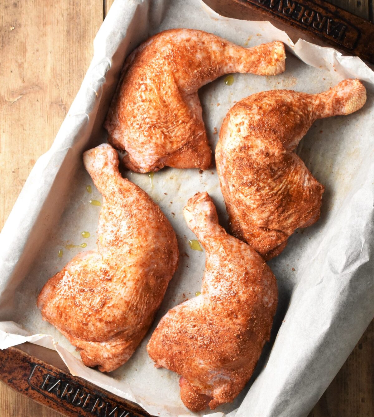 4 spiced chicken leg quarters in roasting pan lined with paper.