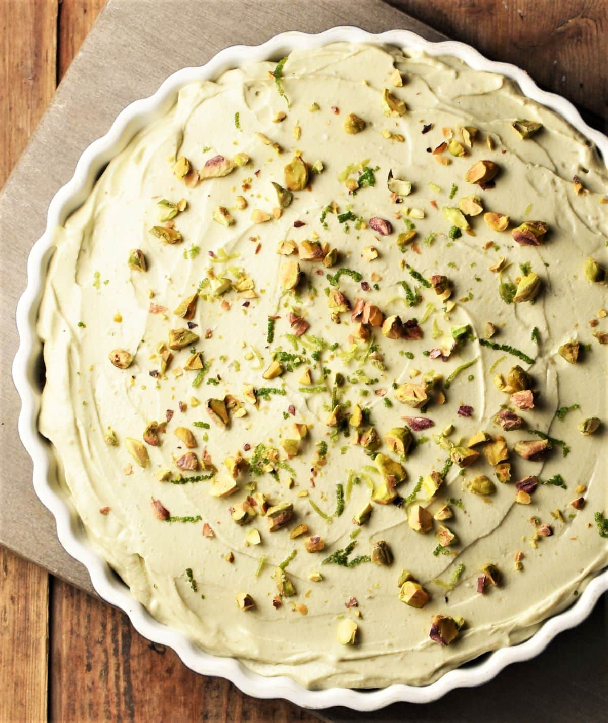Partial view of cheesecake with avocado in pie dish with crushed pistachios on top.