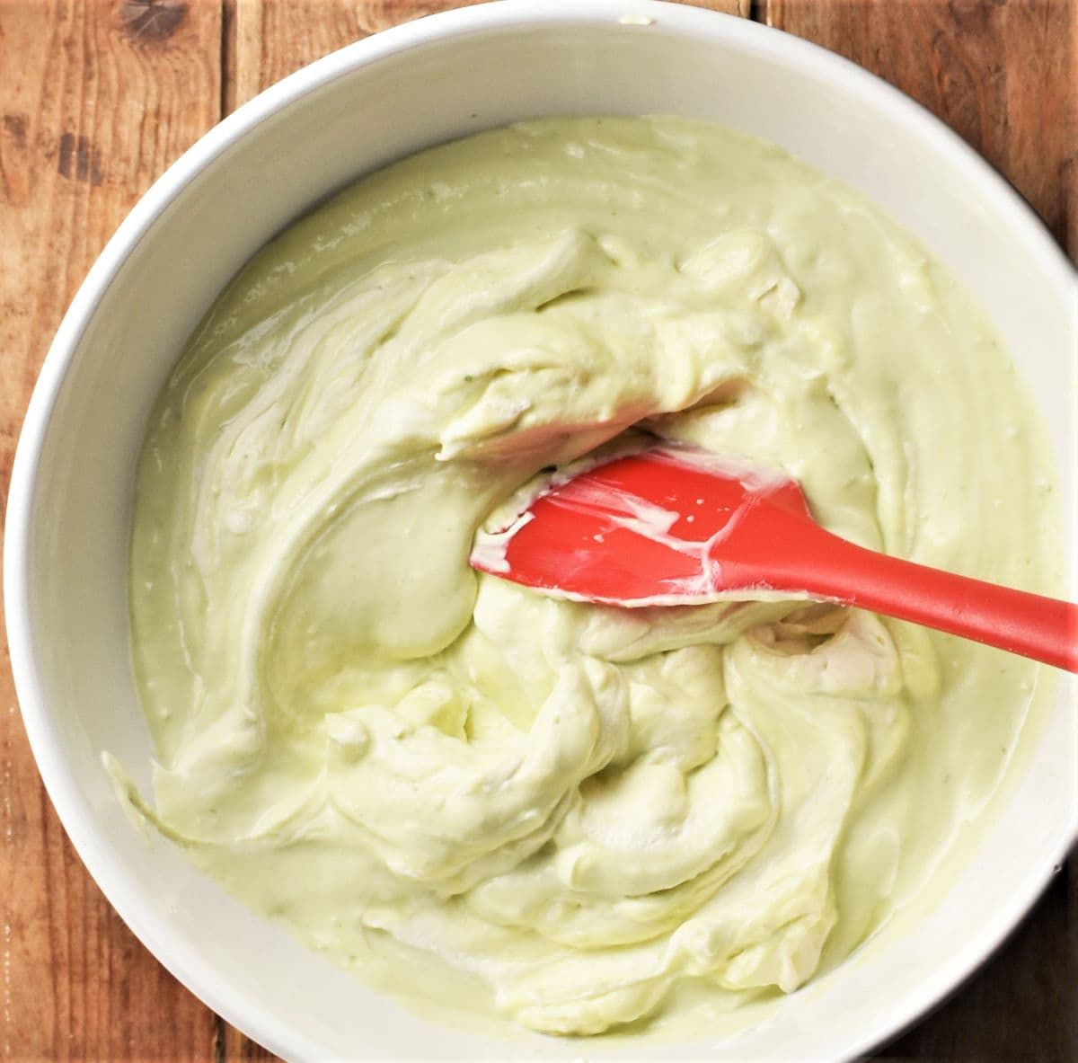 Stirring cheesecake filling mixture in large bowl with red spatula.