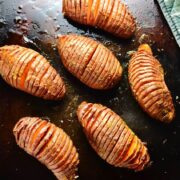 Hasselback sweet potatoes on dark brown oven tray.