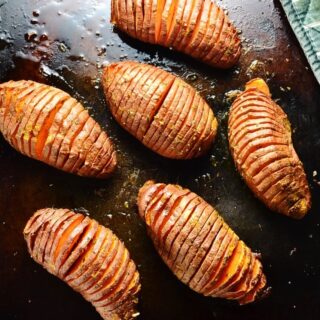 Hasselback sweet potatoes on dark brown oven tray.