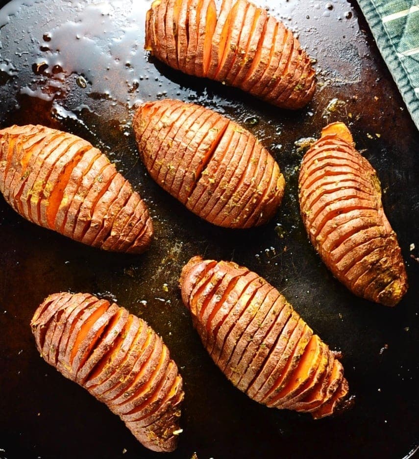 Vegan Hasselback sweet potatoes on dark brown oven tray.