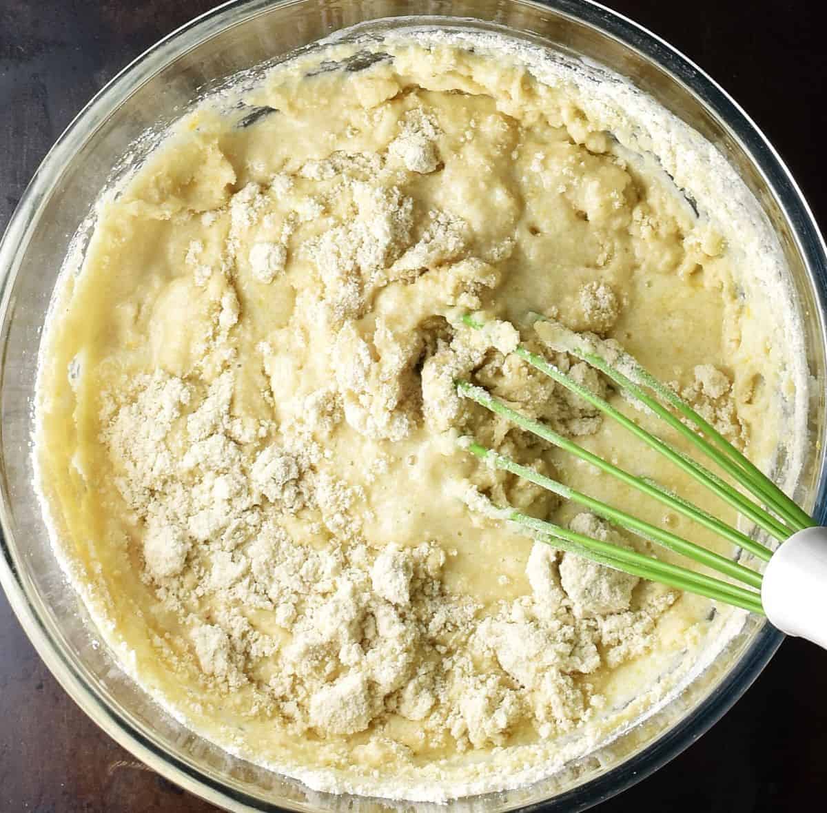Top down view o marzipan muffin batter with dry ingredients visible in bowl with whisk.
