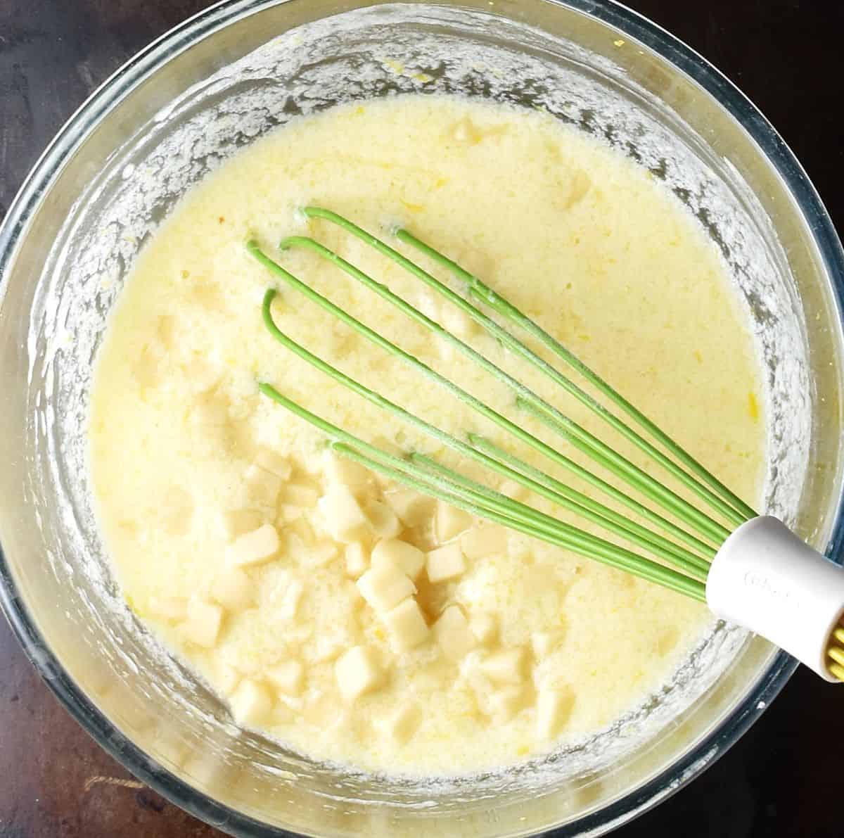 Muffin batter with cubed marzipan and whisk in glass bowl.