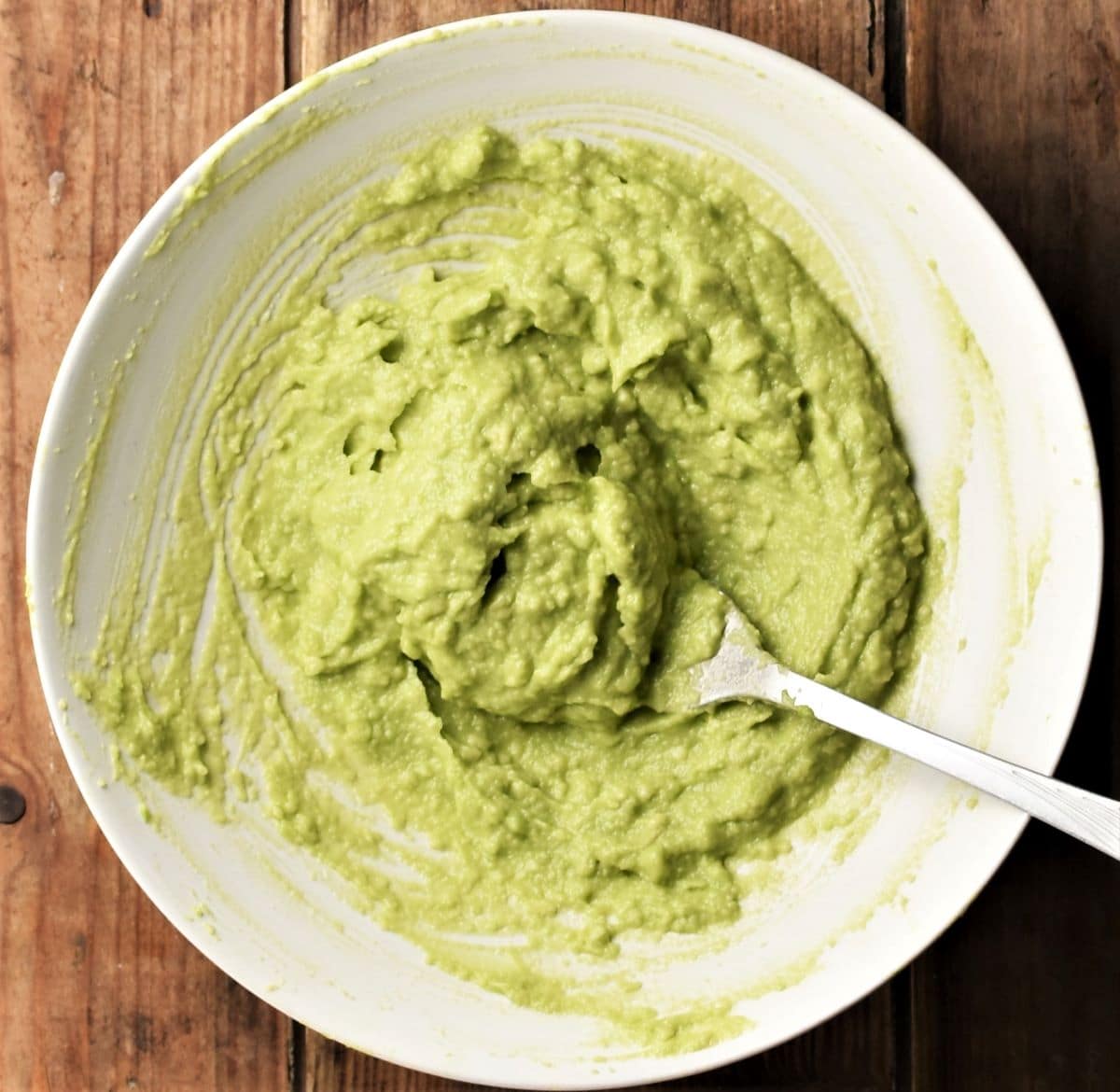 Mashing avocado with fork in white bowl.