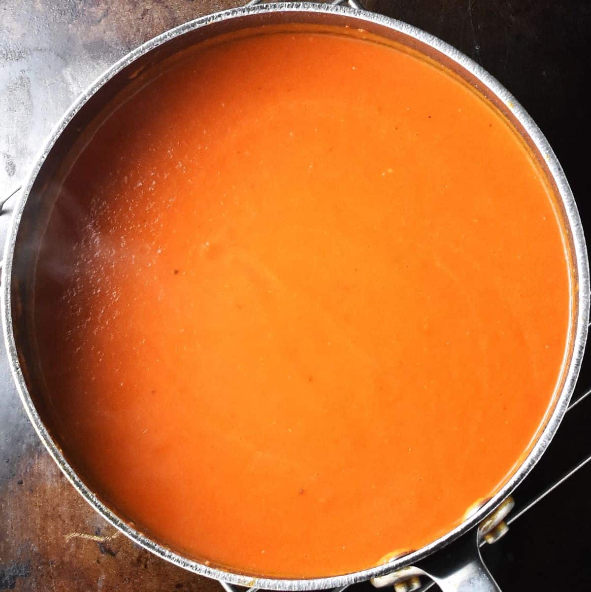 Top down view of creamy tomato red pepper soup in large pot.
