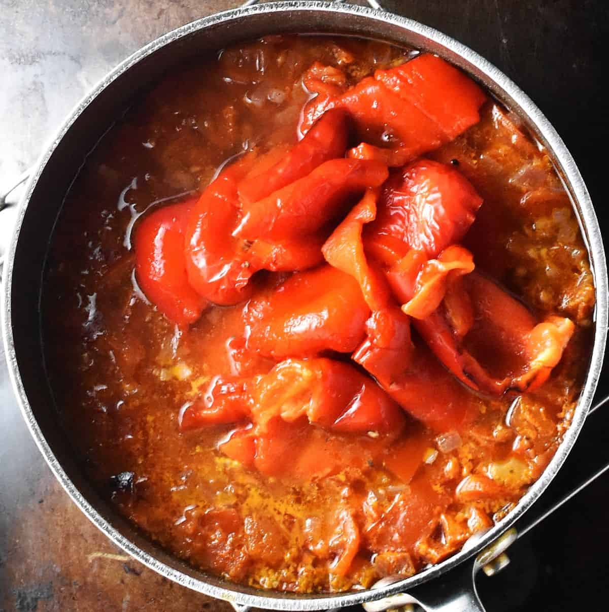 Adding roasted red peppers to tomato soup in pot.