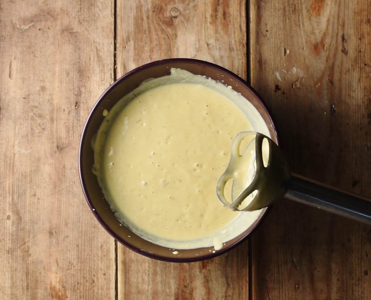 Smooth yellow caesar dressing in purple bowl with stick blender end.