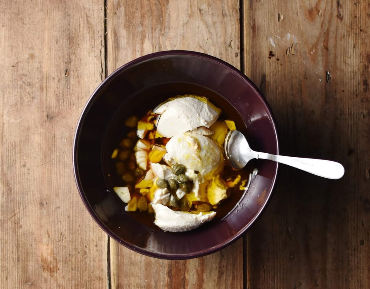 Silken tofu, oil, capers and other ingredients in purple bowl with spoon.
